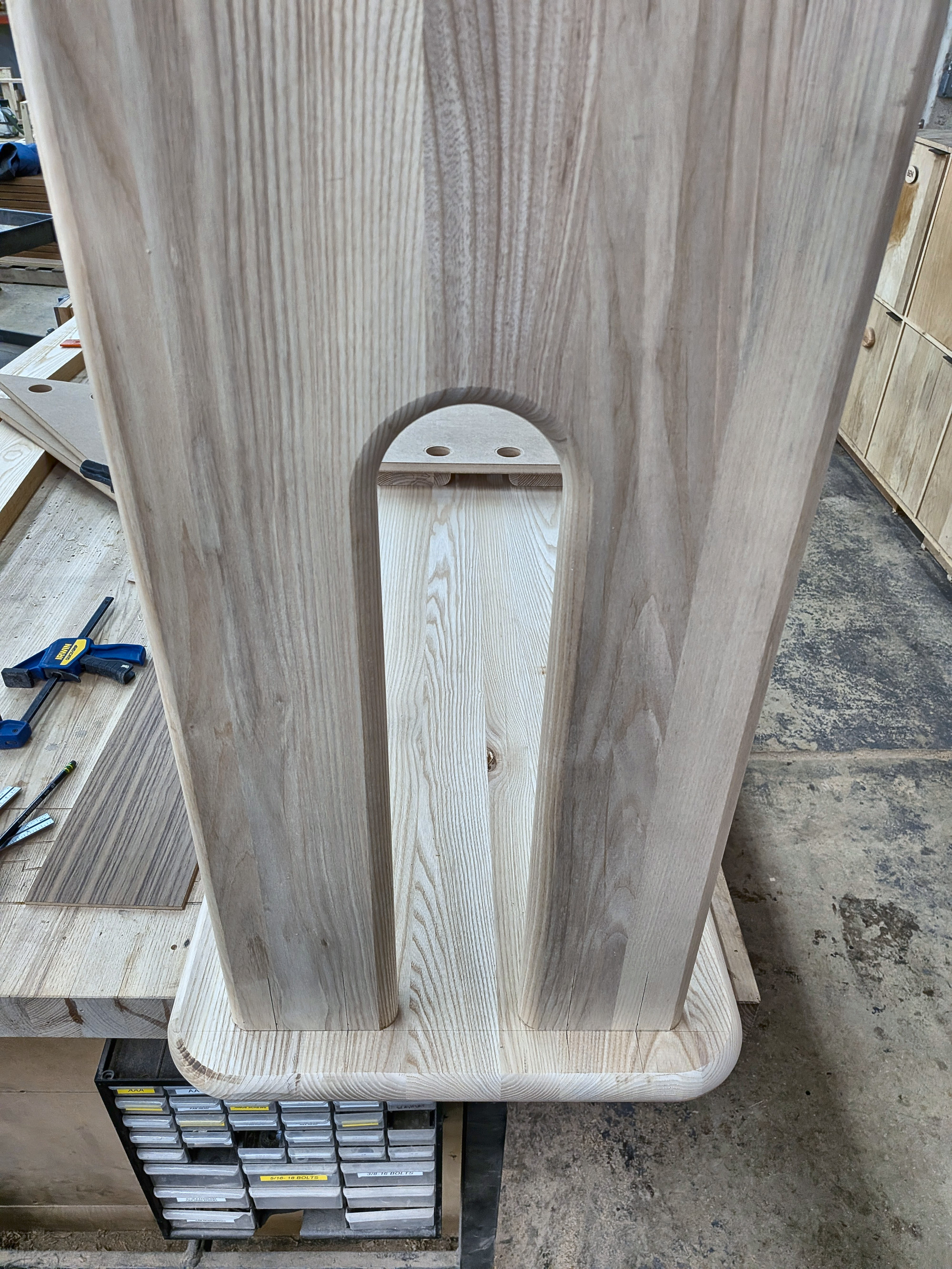 A single machined ash leg standing upright, arched U-shaped cutout visible